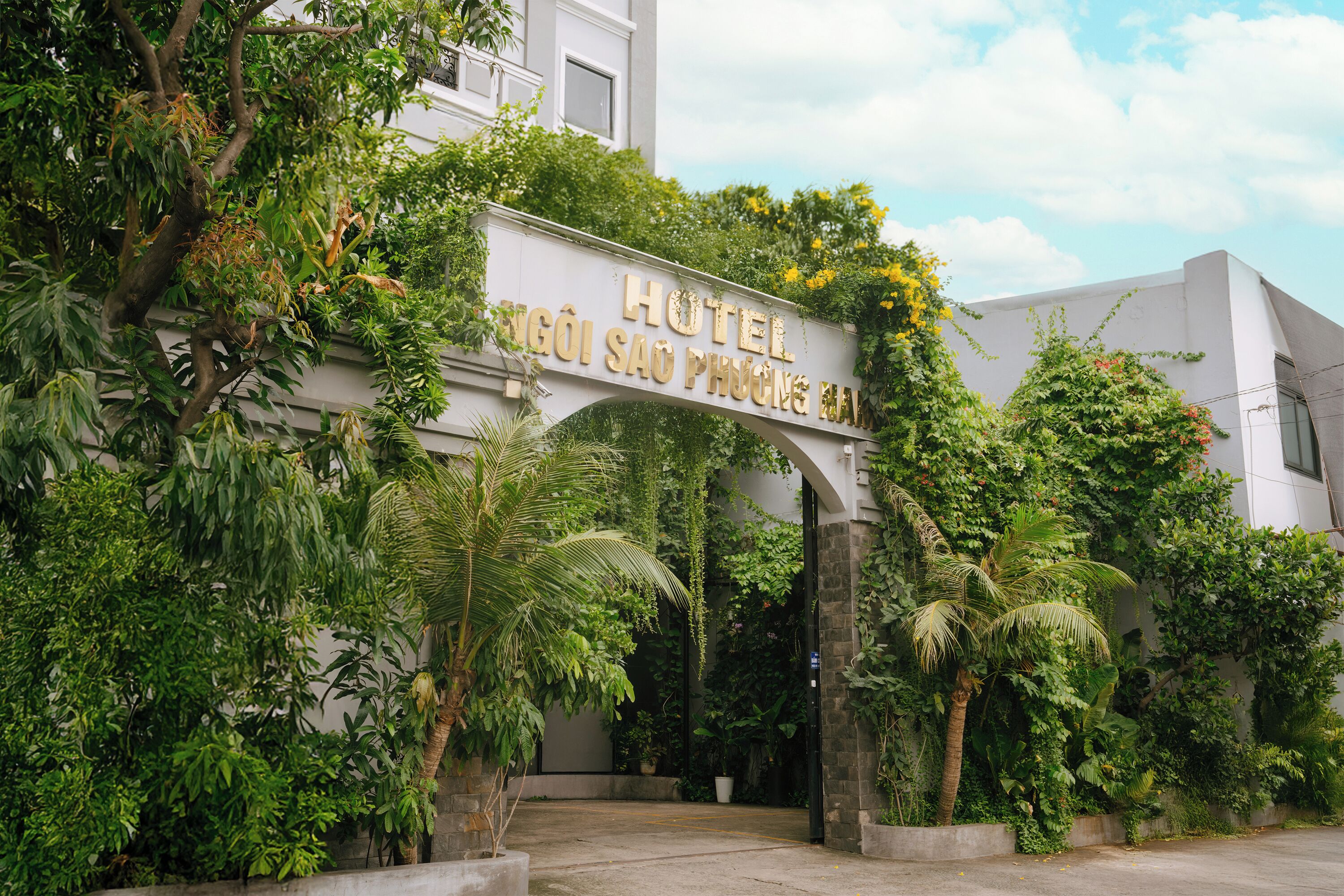 Ein Hotel Eingang mit einem Schild, das "HOTEL HỌI SAO PHƯƠNG HÀN" zeigt, umgeben von üppigem Grün und einem Betonweg.