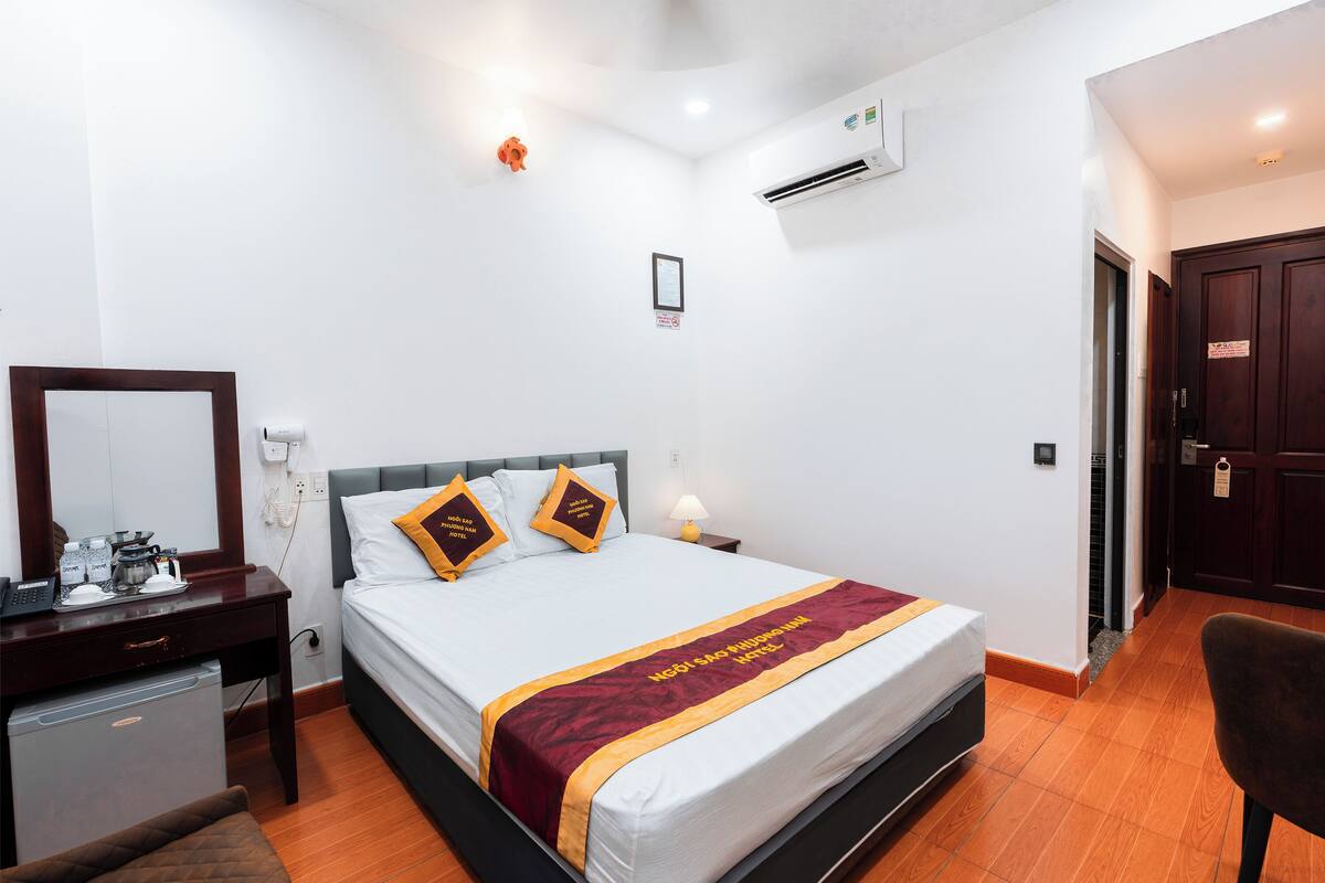 Una habitación de hotel con cama, mesita de noche, lámpara y un escritorio pequeño con cafetera.