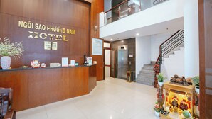Zona de recepción de hotel con un mostrador de madera, una escalera y un pequeño santuario con diversos objetos.