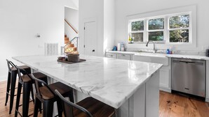 A modern kitchen with a large island, bar stools, a built-in oven, and a window with a view of trees.