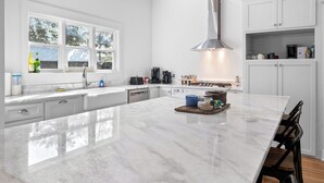 A modern kitchen with a large island, white cabinetry, and a stainless steel range hood.