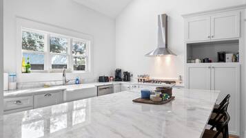 A modern kitchen with a large island, white cabinetry, and a stainless steel range hood.