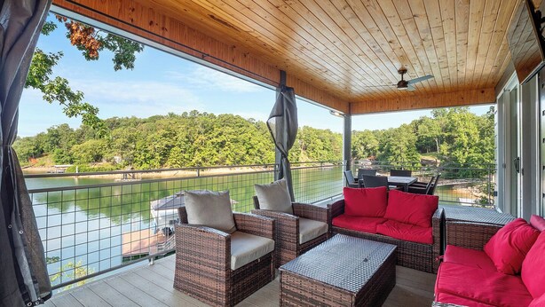 A covered outdoor seating area with wicker furniture, a red sofa, and a view of a lake and forest.