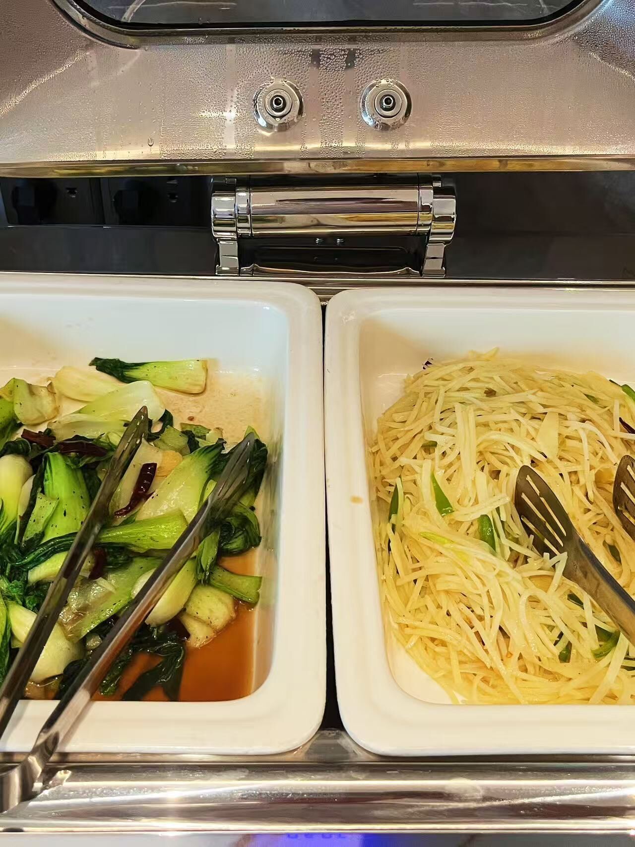 Twee witte kommen met eten, één met paksoi en de andere met noedels, op een oppervlak van roestvrij staal.