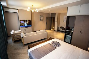 Una habitación de hotel moderna con una cama grande, un sofá, un televisor, una kitchenette y un comedor.