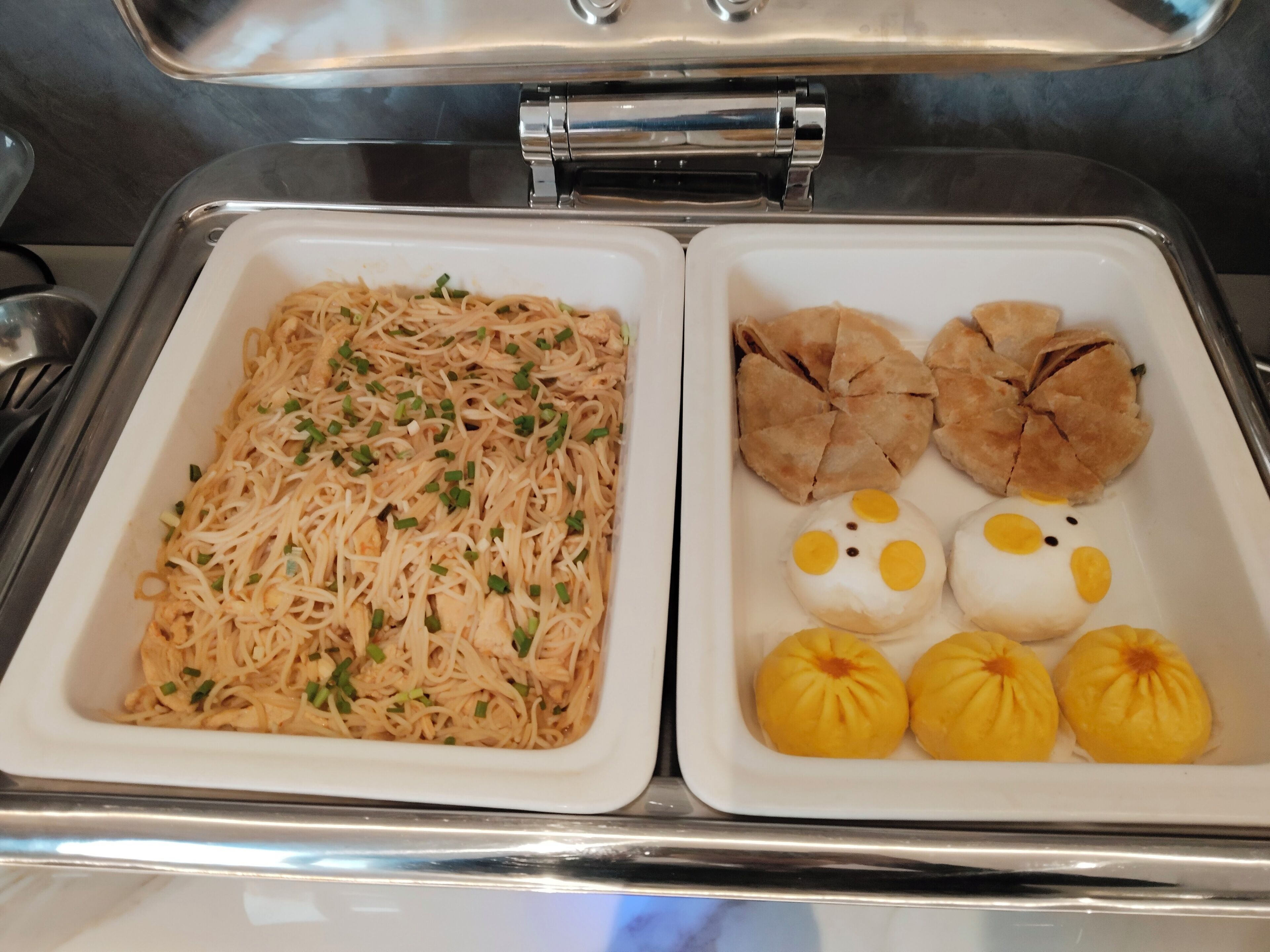 Ein Buffet mit zwei Tabletts: eines mit Nudeln, das andere mit Gebäck und Brötchen.