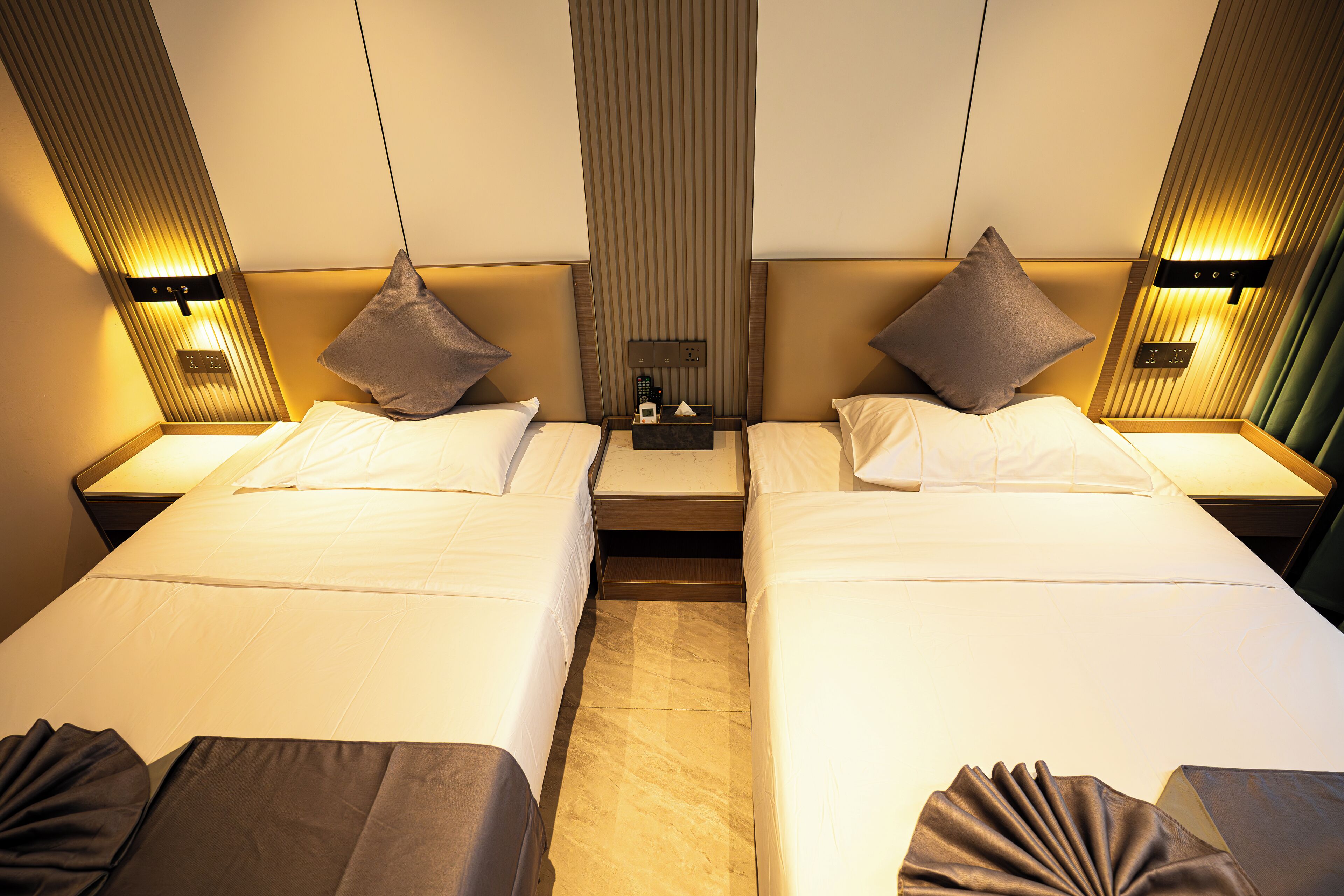 Ein Hotelzimmer mit zwei Betten, jeweils mit einem Kissen und einem Nachttisch mit einer Lampe.