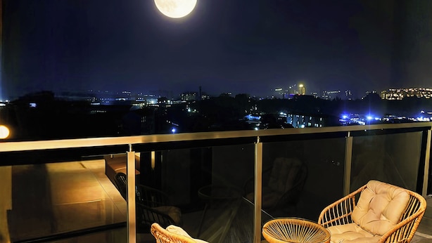 Un balcon avec deux fauteuils en osier et une vue sur le paysage urbain illuminé la nuit.