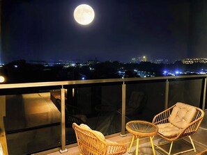 Un balcon avec deux fauteuils en osier et une vue sur le paysage urbain illuminé la nuit.