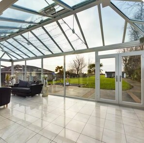 A conservatory with a glass roof, a tiled floor, and a seating area with a sofa and a table. - Beautiful house in Blackpool - 10 minutes from the beach (Blackpool)