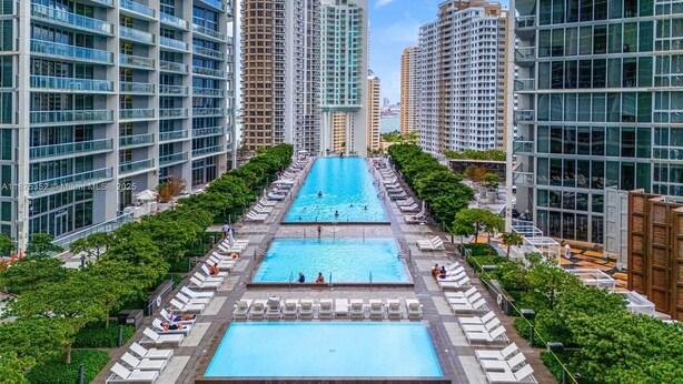 A modern high-rise building with a central swimming pool surrounded by lounge chairs and greenery. - Miami Brickell Condos (Miami)