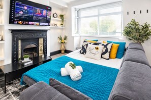 Una habitación de hotel moderna con chimenea, una cama con colcha azul y un televisor mostrando contenido deportivo.