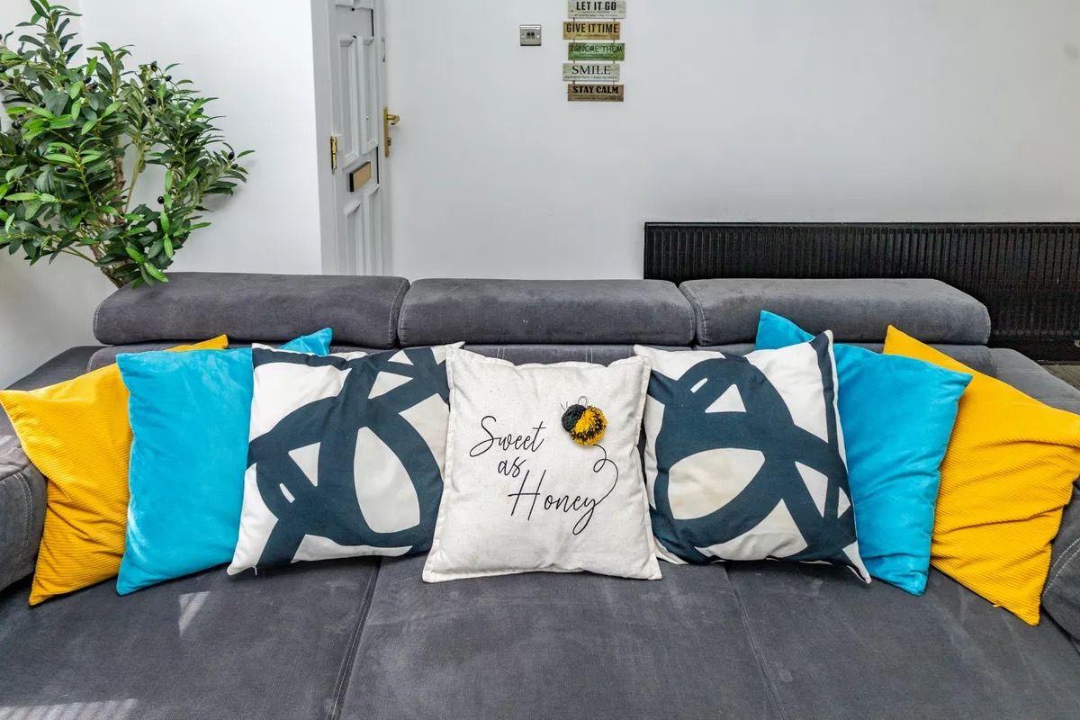 A grey sofa with multiple cushions, including a central pillow with a honeycomb design and the text 'Sweet as Honey.'