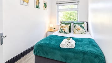 A hotel room with a bed, a window, a nightstand, and wall art.