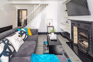 Un salón moderno con un sofá gris, una mesa de centro negra, una chimenea y un televisor montado en la pared.