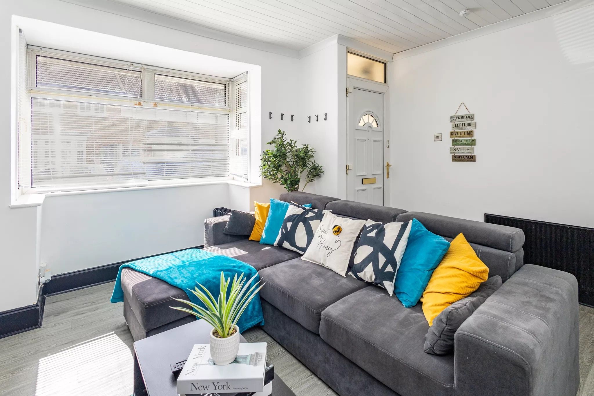 En moderne stue med en grå sofa, farverige puder, en lille plante og en bog med titlen 'New York'.