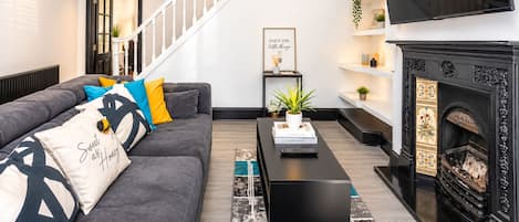 A modern living room with a grey sofa, a black coffee table, a fireplace, and a staircase.