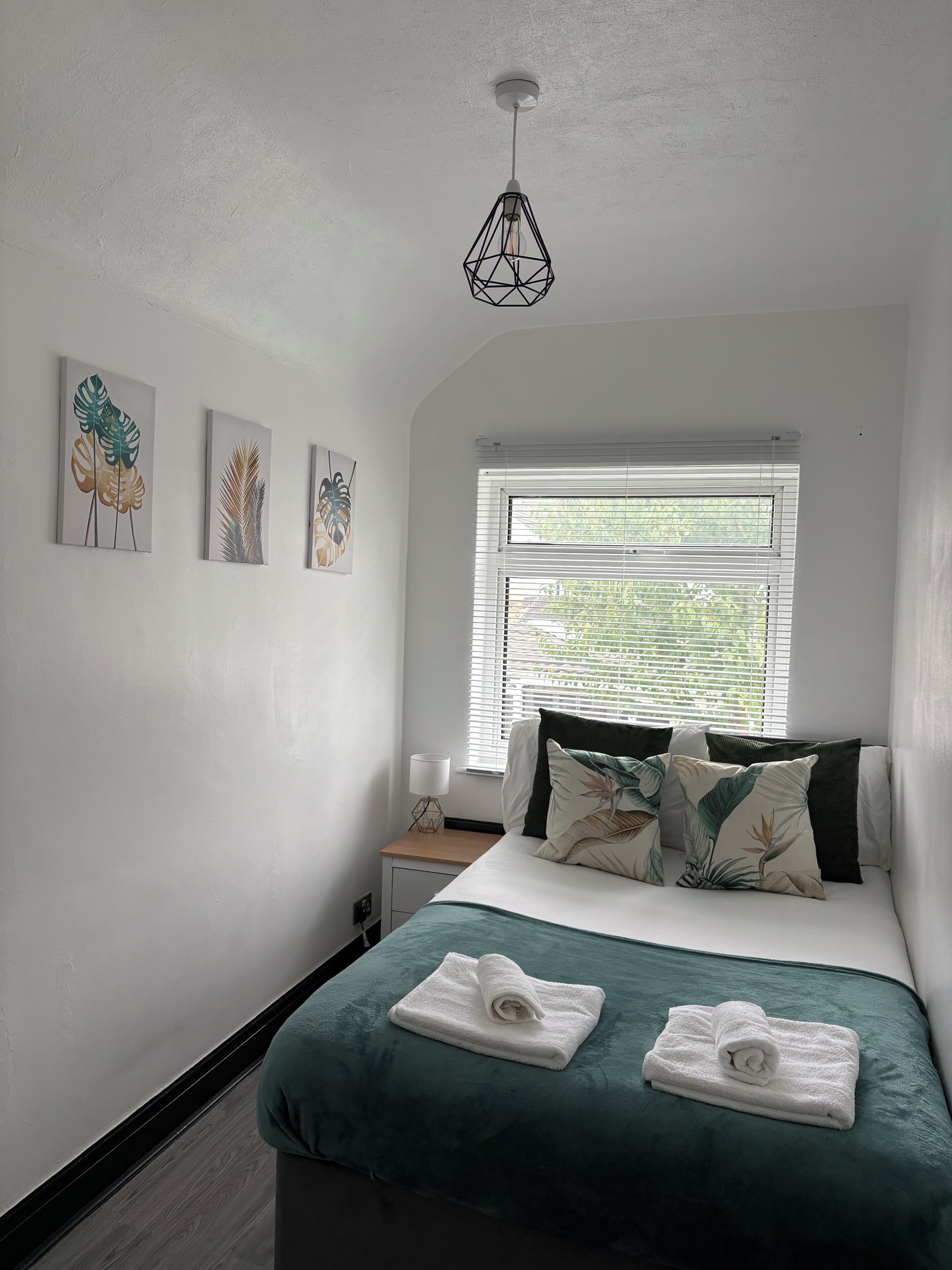 A bedroom with a bed, a bedside table, a lamp, and a window with blinds.