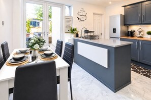 A modern kitchen with a central island, dark cabinetry, and a dining area with a white table set for four.