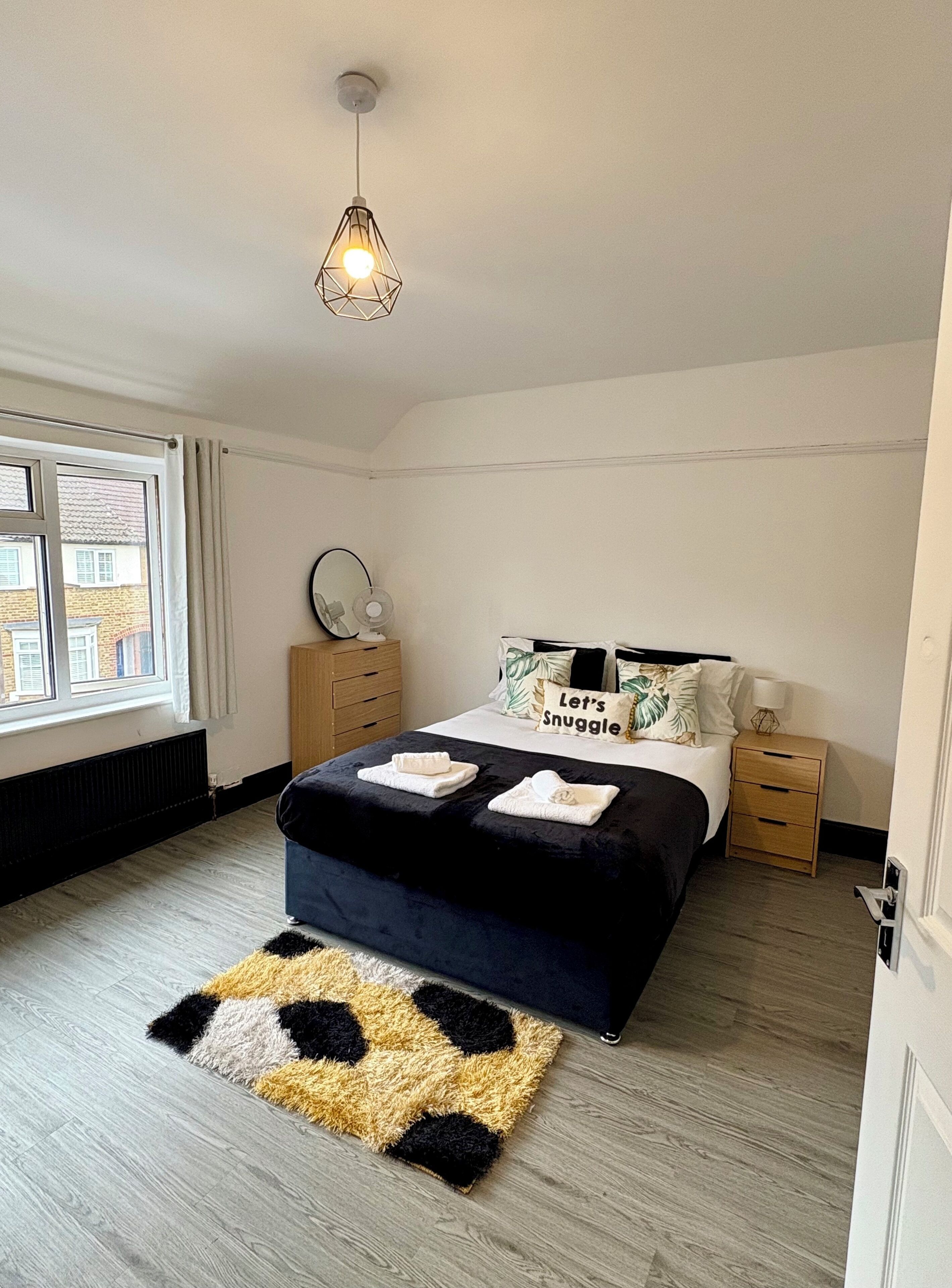 A bedroom with a bed, bedside tables, a mirror, a window, and a ceiling light.
