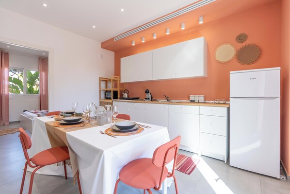 A modern kitchen with white cabinets, a white refrigerator, and a dining area with a table set for four.