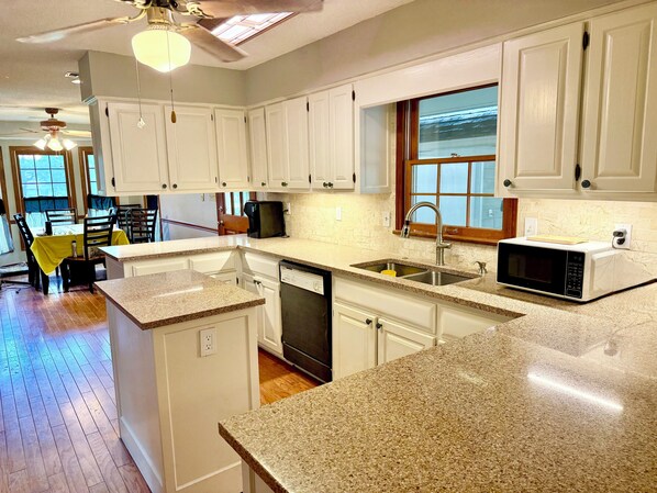A kitchen with white cabinets, a granite countertop, a dishwasher, a sink, and a microwave.