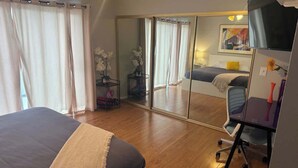 Un dormitorio con una cama, un escritorio, una silla, un espejo y un armario.