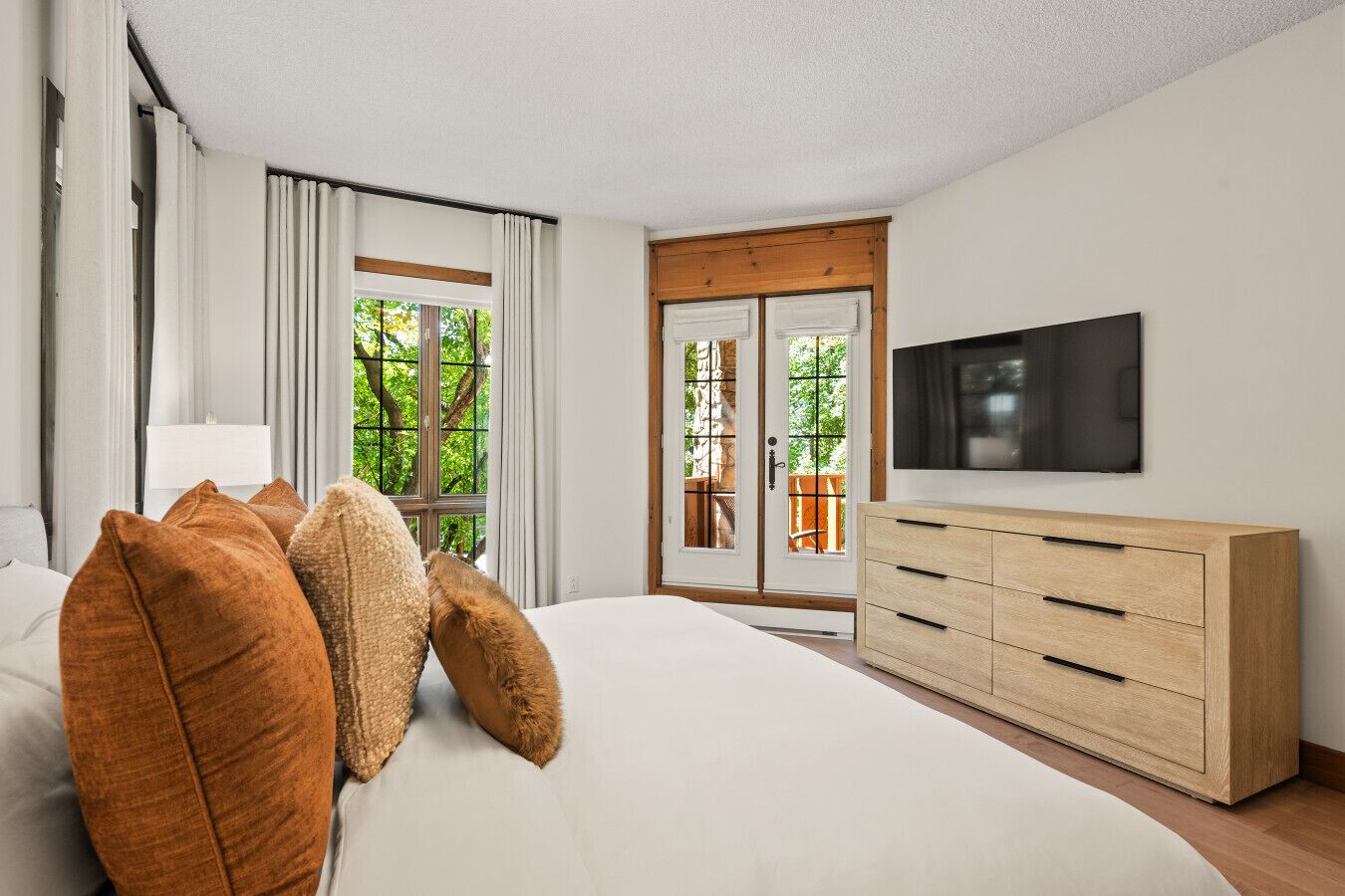Une chambre d’hôtel dotée d’un grand lit, d’une commode en bois, d’un téléviseur à écran plat et d’une porte-fenêtre coulissante donnant sur un espace extérieur.