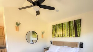 Una habitació amb un llit, una taula de nit, un fanal de sostre, un mirall i una planta penjada a la paret.