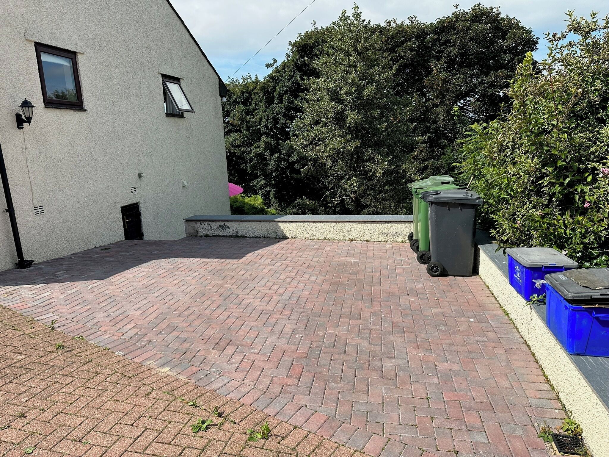 A paved courtyard with a white building, green bins, and a blue bin.