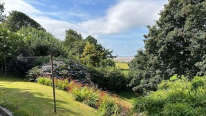 A landscaped garden with a variety of plants and flowers, a pathway, and a view of the sea in the background. - The Rookery Sandside-Stylish Luxury Home (Kirkby in Furness)