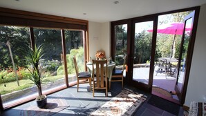 Une pièce dotée d’une grande porte-fenêtre coulissante qui donne sur un patio extérieur. À l’intérieur, on trouve une table à manger avec des chaises, une plante en pot et un tapis.