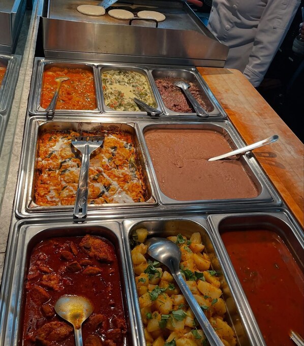 Un buffet proposant divers plats, notamment des pâtes, une sauce brune et une sauce rouge.