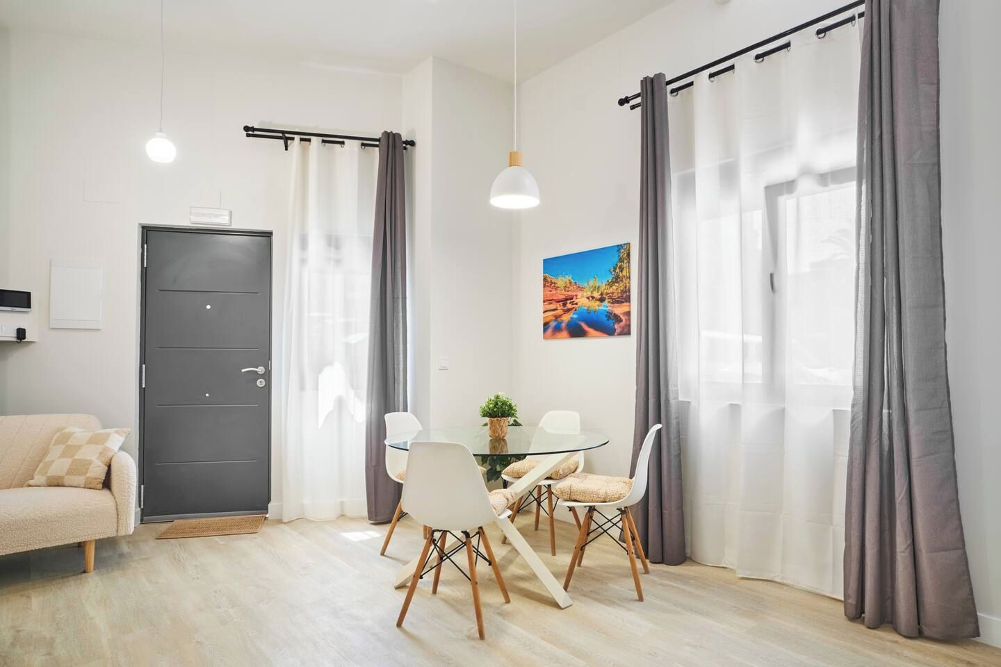 Un salón moderno con una mesa de comedor de vidrio, sillas blancas, una puerta gris y cortinas grises.