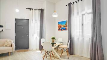 Un salón moderno con una mesa de comedor de vidrio, sillas blancas, una puerta gris y cortinas grises.