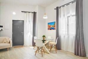 A modern living room with a glass dining table, white chairs, a grey door, and grey curtains.