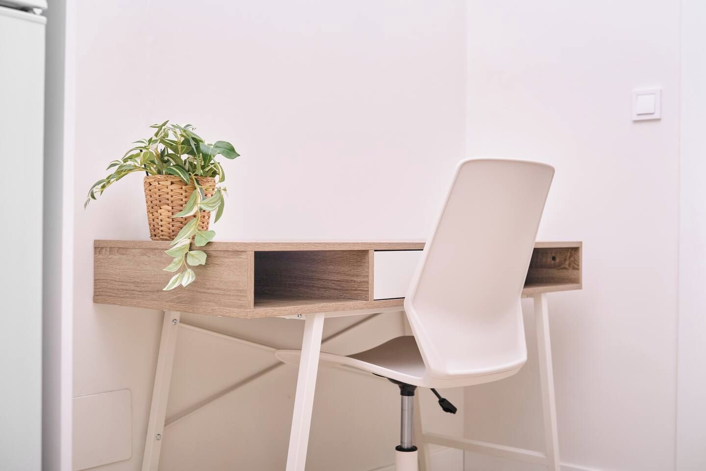 Un espacio de trabajo con una silla blanca, un escritorio de madera y una planta en maceta.