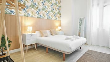 Un dormitorio moderno con una cama grande, mesitas de noche, un cabecero de madera y un papel tapiz con estampado de hojas tropicales.