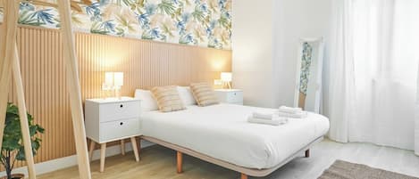 A modern bedroom with a large bed, bedside tables, a wooden headboard, and a tropical leaf-patterned wall.