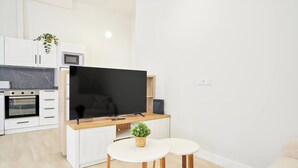 A modern kitchen with a built-in oven, microwave, and a flat-screen TV. There are two white tables with wooden legs and a small potted plant on the counter.