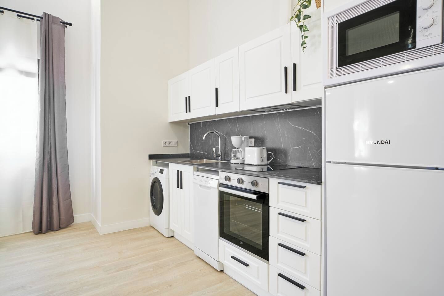 Una cocina moderna con lavadora, horno, microondas y cafetera sobre la encimera.