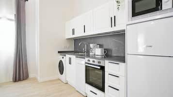 Una cocina moderna con lavadora, horno, microondas y cafetera sobre la encimera.