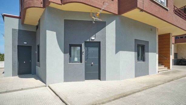 A modern building with a grey facade, a central door, and a small window.