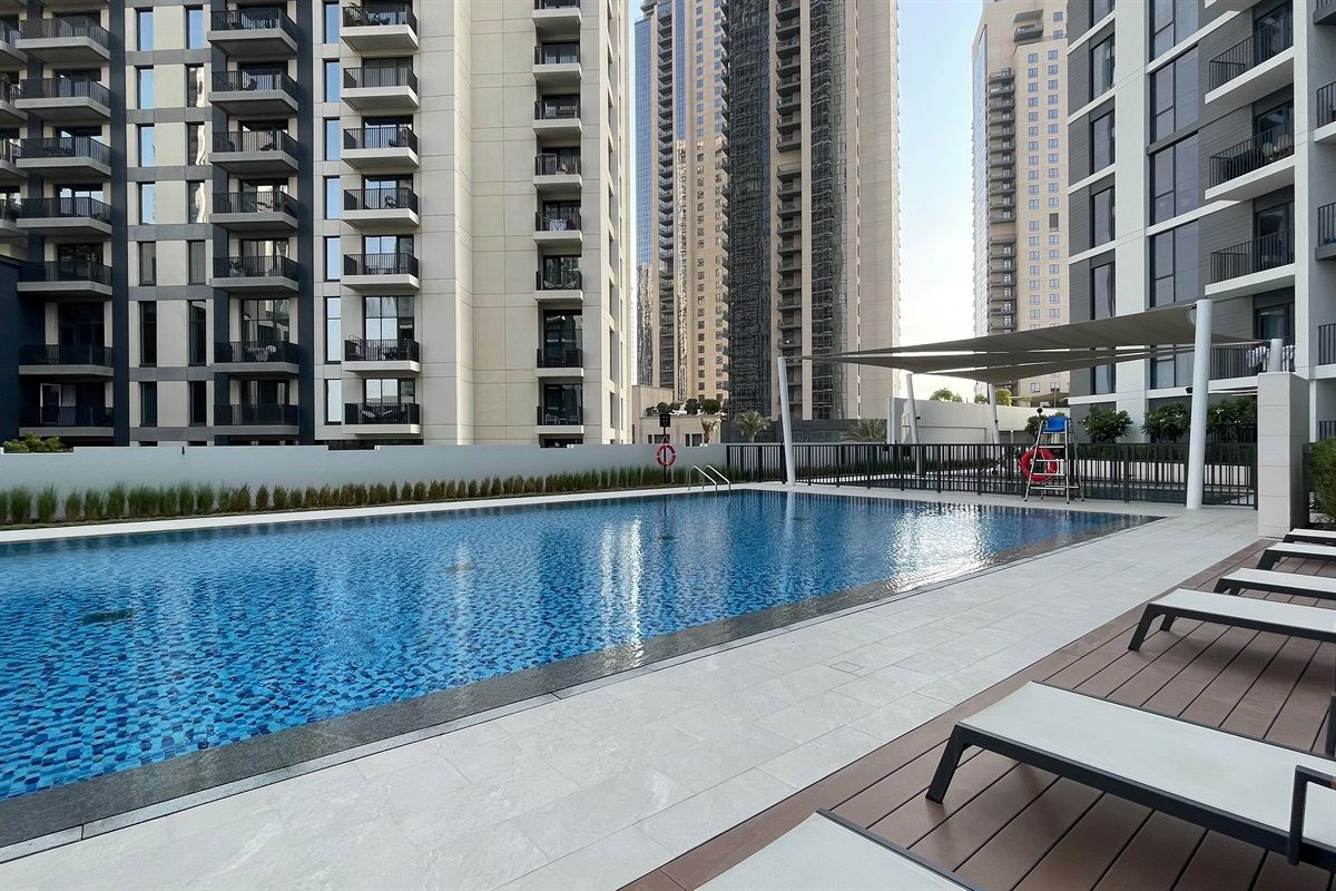 Una piscina con sillas de descanso y una cerca, rodeada de edificios residenciales altos.