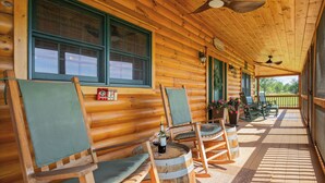 Una cabaña de troncos con un porche, sillas de madera, una mesa y una botella, y vistas al exterior.