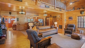 A spacious wooden interior with a high ceiling, a central seating area with a sofa and chairs, and a staircase leading to an upper level.