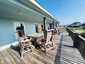 Una terraza de madera con una mesa y sillas, un espacio cubierto con barandilla, y vistas del entorno.