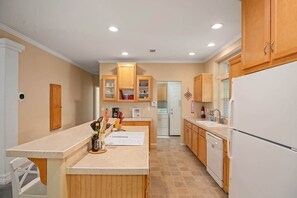 Une cuisine avec des meubles de rangement en bois, un réfrigérateur blanc et un plan de travail sur lequel sont posés des ustensiles de cuisine.