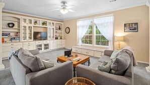 A living room with a sofa set, a coffee table, a television, and a window with curtains. - Guadalupe Riverfront Retreat | Sleeps 10 Kerrville (Kerrville)