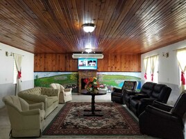 Quarto aconchegante com teto e paredes de madeira, apresentando uma lareira, uma televisão e assentos confortáveis.
